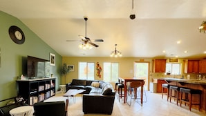 A spacious living area with a sofa, coffee table, and a TV on a stand. There is a dining area with a table and chairs, and a kitchen with wooden cabinets and a bar.