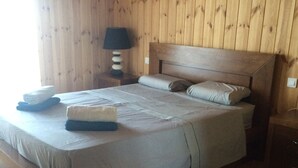 A wooden-paneled room with a bed, pillows, a nightstand, a lamp, and a bench.
