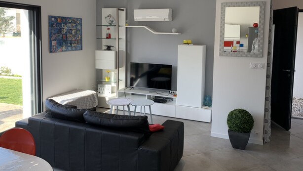 Ein modernes Wohnzimmer mit einer schwarzen Ledersofa, einem Esstisch mit roten Stühlen, einem Flachbildfernseher und einer integrierten Küchenzeile.