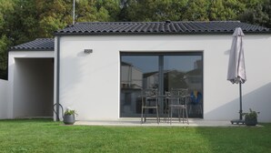 Ein modernes Haus mit einer Terrasse, auf der sich Tisch und Stühle befinden, einer Schiebetür und einer überdachten Sitzgelegenheit im Freien.