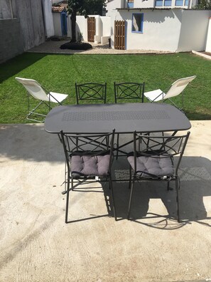 A patio table with four chairs, a small tree, and a white building with blue accents in the background. - Charming new house in La Rochelle (La Rochelle)