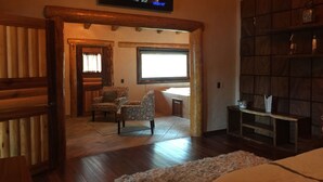 Una habitación acogedora con suelo de madera, un ventanal grande, un televisor montado en la pared y una estantería.