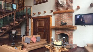 Amplia sala de estar con chimenea, cabeza de animal montada, televisor y escalera.