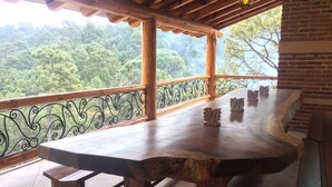 Una mesa de madera con bancos, un balcón con barandilla de hierro forjado y vistas a un paisaje boscoso.