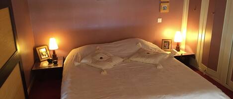 Een opgemaakt bed met kussens, twee bedlampen en een lijst op het nachtkastje.