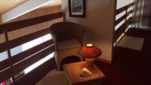 Une pièce chaleureuse avec un plafond en bois, un fauteuil en osier, une petite table avec une lampe et un tableau encadré au mur.