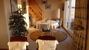 Un coin repas comprenant une table ronde, des chaises, un escalier et une grande fenêtre avec des rideaux.
