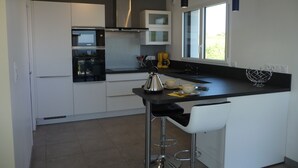 Une cuisine moderne avec des meubles blancs, un plan de travail noir, des appareils en acier inoxydable et un tabouret de bar.