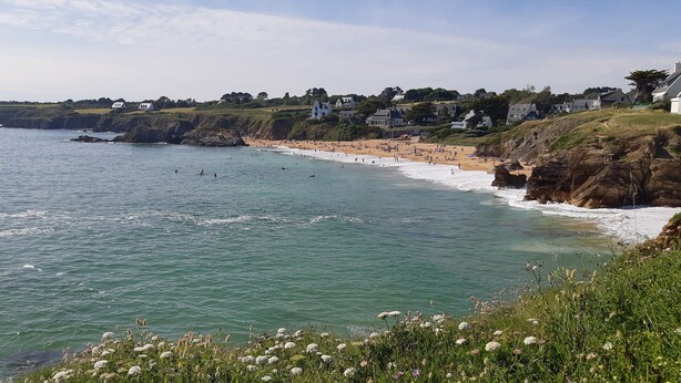 Une plage côtière bordée de maisons construites sur le flanc d’une colline et d’une côte rocheuse.