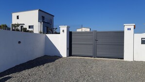 Une entrée fermée par un portail donnant accès à un immeuble moderne à la façade blanche et au portail noir.