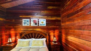 A wooden cabin bedroom with a bed, two bedside tables, and three framed pictures on the wall.