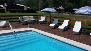 A swimming pool with a wooden deck, lounge chairs, and umbrellas.