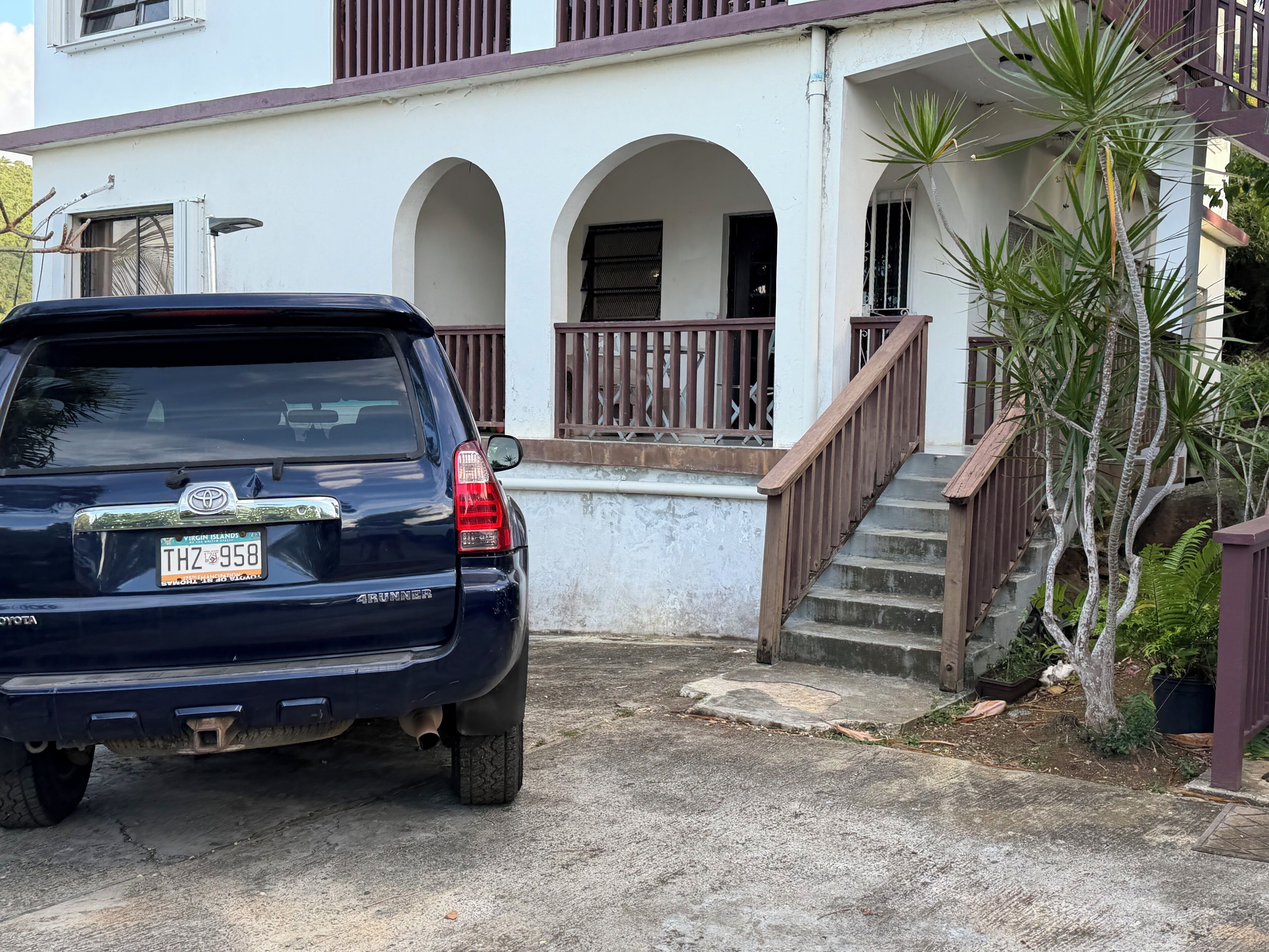 Un SUV nero parcheggiato di fronte a un edificio bianco con un balcone e una scalinata.
