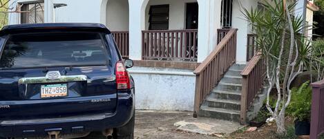 Un SUV nero parcheggiato di fronte a un edificio bianco con un balcone e una scalinata.