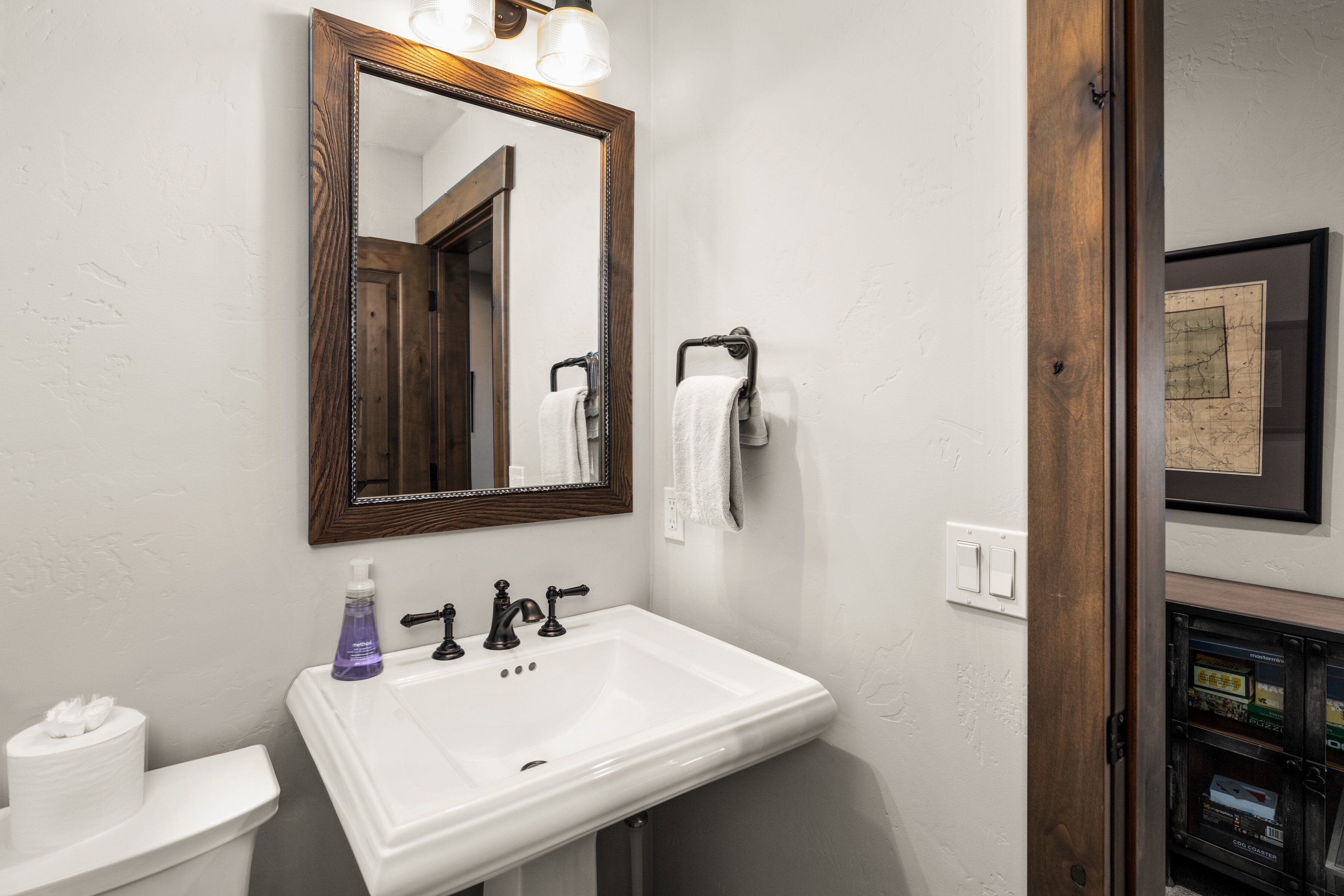 Un baño con lavamanos blanco, un espejo con marco de madera y un perchero para toallas.