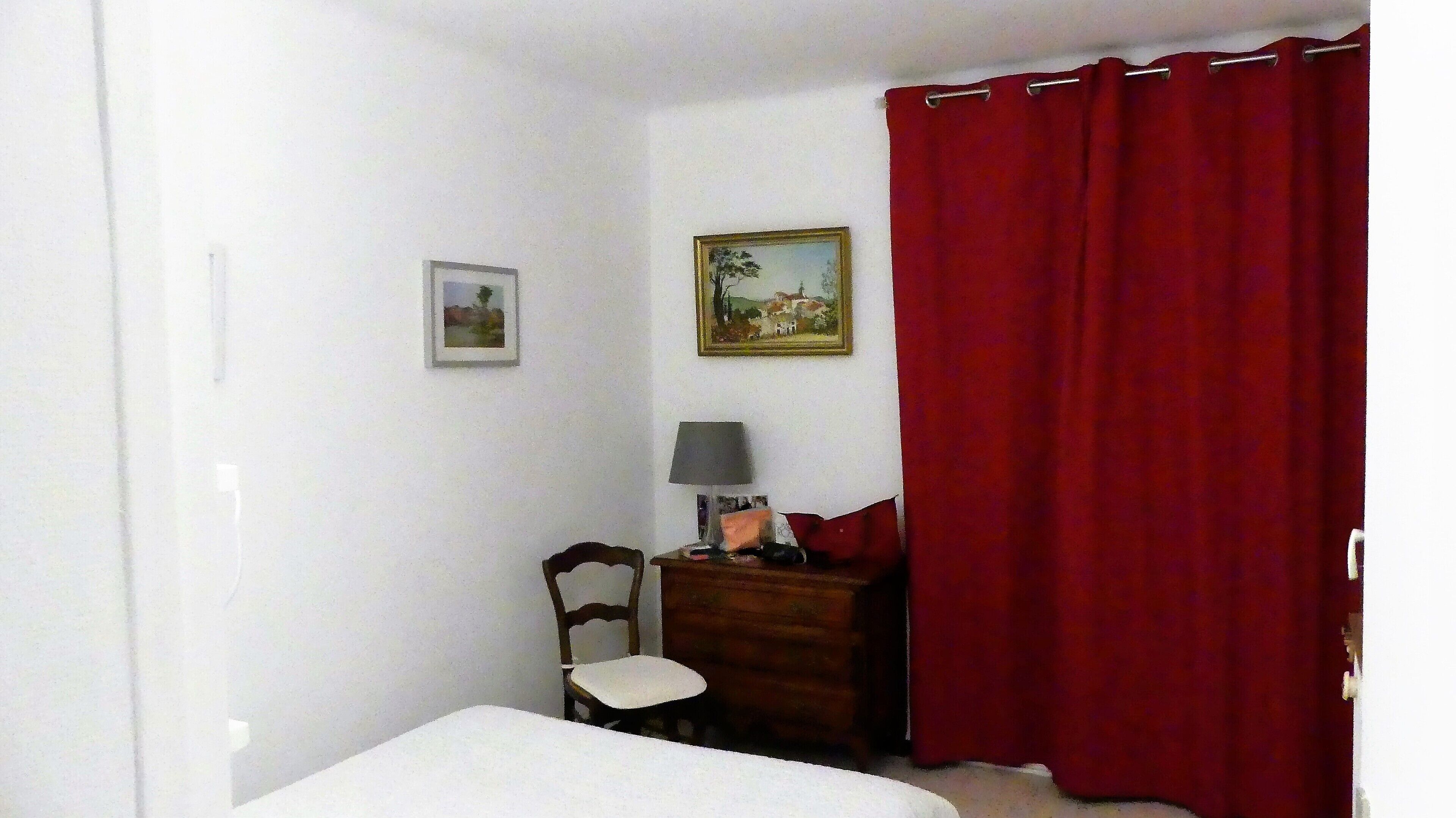 Een slaapkamer met een bed, een stoel, een dressoir, een lamp en twee schilderijen aan de muur.
