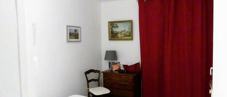 Een slaapkamer met een bed, een stoel, een dressoir, een lamp en twee schilderijen aan de muur.