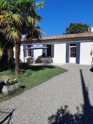 A white building with a tiled roof, a gravel driveway, a palm tree, and outdoor furniture.