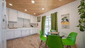 Une cuisine moderne avec des meubles blancs, un plafond en bois et un coin repas avec des chaises vertes et une table en verre.