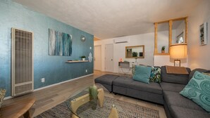 Un salon moderne avec un mur d’accent bleu, un canapé gris, une table basse en verre et un banc en bois.