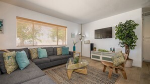 Un salon avec un canapé d’angle gris, une table basse en verre, un téléviseur et une grande plante en pot.