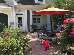Eine Terrasse mit Tisch und Stühlen, umgeben von Topfpflanzen und einem roten Sonnenschirm.