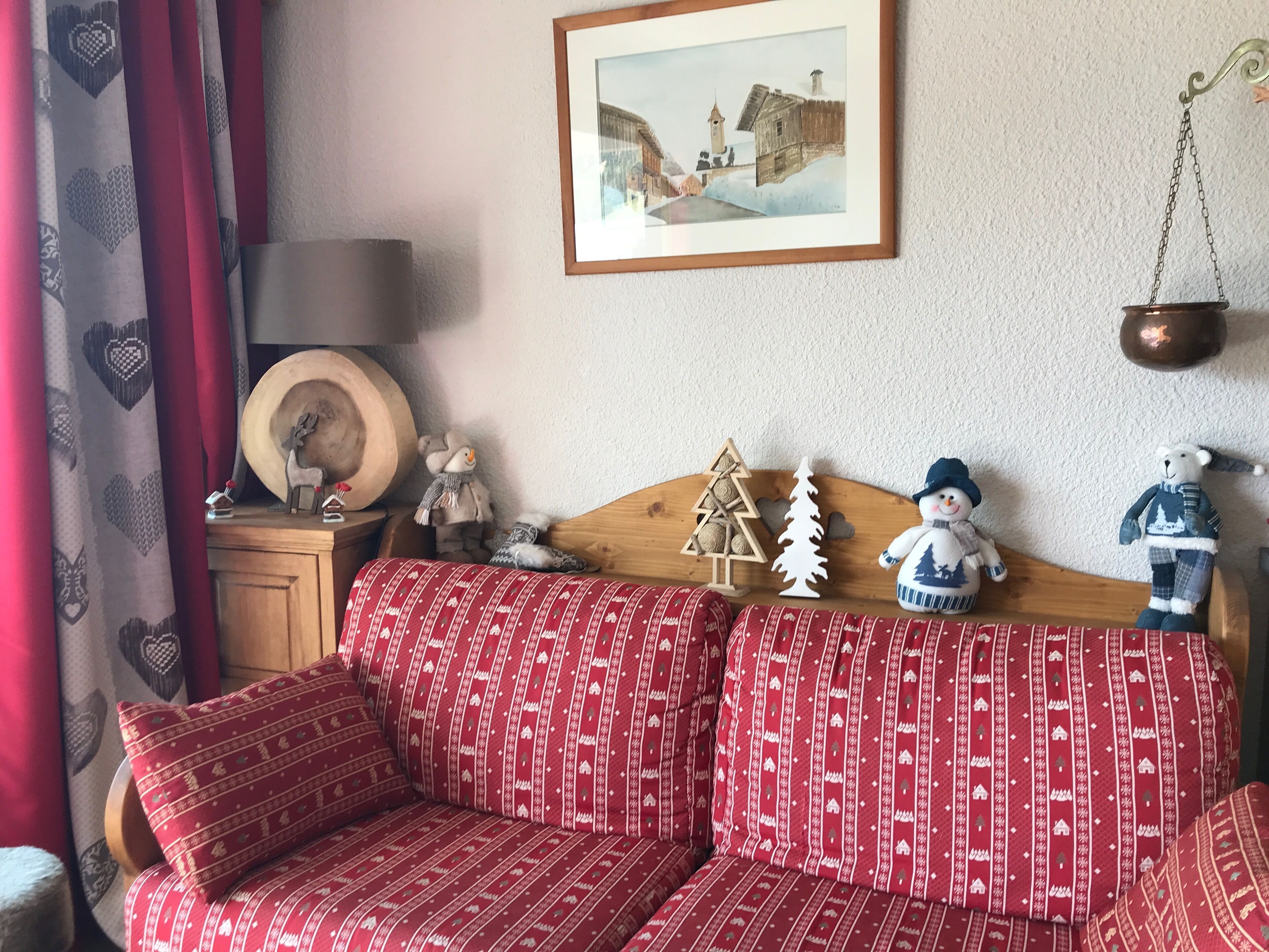 Una sala de estar acogedora con un sofá rojo estampado, una mesita de madera con adornos, un cuadro enmarcado en la pared y una lámpara colgante.
