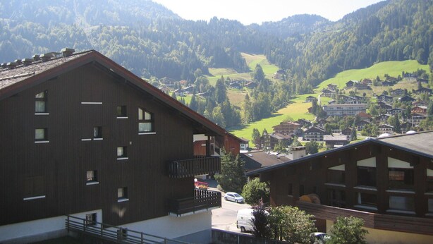 Un bâtiment doté de nombreuses fenêtres et de balcons, entouré d ’un paysage montagneux avec un village situé dans la vallée.
