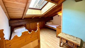 Une chambre mansardée chaleureuse, avec un plafond en pente, un puits de lumière, un lit en bois, un petit banc et une table de chevet.