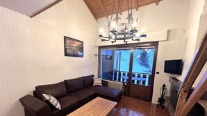 Un salon chaleureux avec un canapé en cuir marron, une table basse en bois et un lustre. On y trouve une cheminée et un téléviseur fixé au mur.