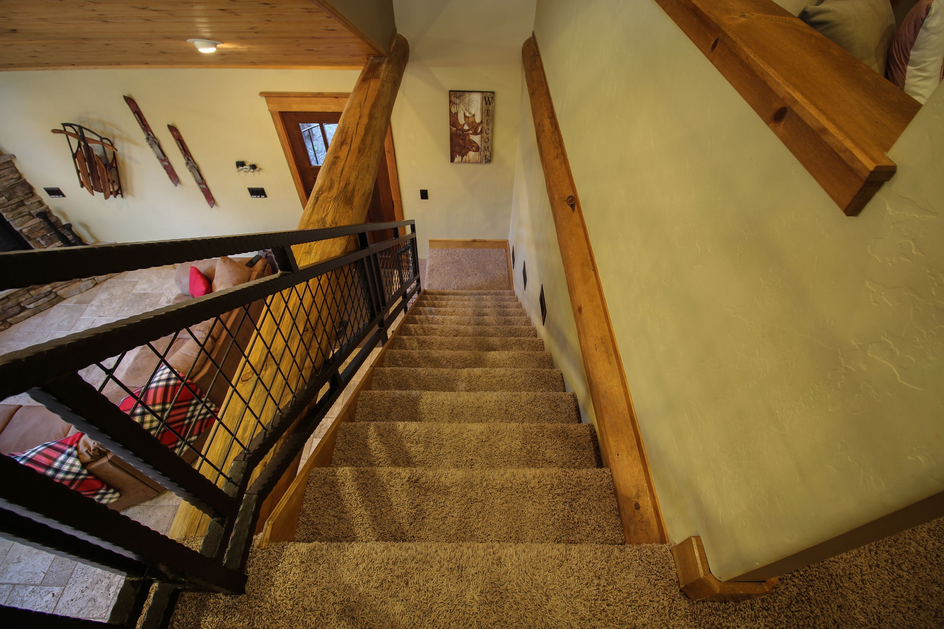 A carpeted staircase with wooden railings and a view of a room with a plaid blanket and pillows.