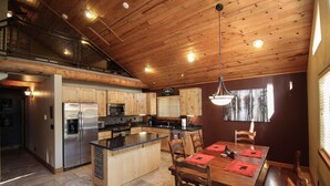 A spacious kitchen with a wooden ceiling, a central island, and a dining area with wooden furniture. - Beautiful Wooded Dream Cabin Backs Forest (Flagstaff)