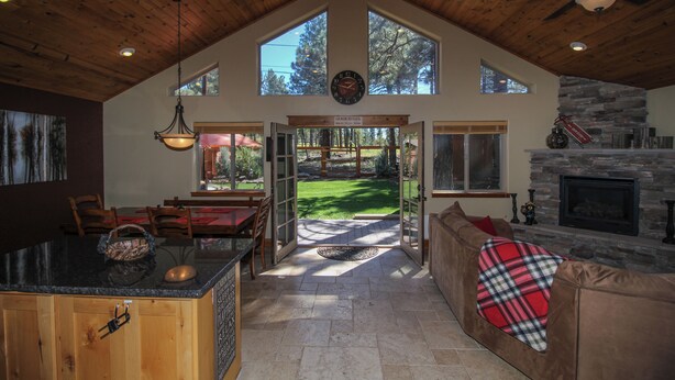 A spacious living area with a stone fireplace, wooden ceiling, and large windows. - Beautiful Wooded Dream Cabin Backs Forest (Flagstaff)