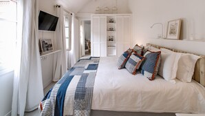 Une chambre avec un grand lit, un téléviseur fixé au mur, une armoire avec un miroir et une étagère avec des photos encadrées.