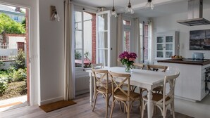 Une cuisine lumineuse avec des meubles blancs, une table à manger en bois et une vue sur un jardin, visible à travers des portes ouvertes.