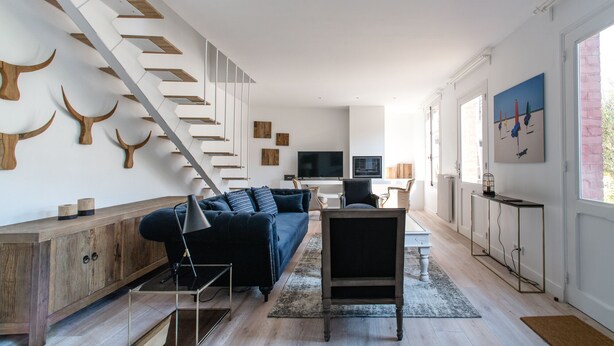 Un salon moderne avec un escalier, un canapé, un téléviseur et un coin repas.