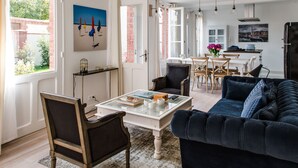 Un salon avec un canapé bleu foncé, une table basse en bois et un coin repas comprenant une table et des chaises blanches.