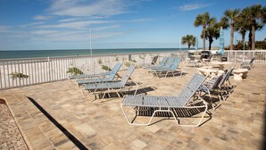 A beachside patio with sun loungers and tables, overlooking the ocean. - Beachfront steps to beach with Remodeled Kitchen, Quartz Countertops (Indian Rocks Beach)