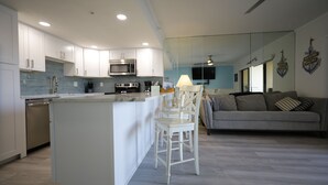A modern kitchen with white cabinetry, a built-in microwave, and a central island with bar stools. - Beachfront steps to beach with Remodeled Kitchen, Quartz Countertops (Indian Rocks Beach)
