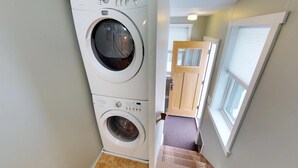 Une buanderie équipée d’un lave-linge et d’un sèche-linge à chargement frontal, d’une porte en bois et d’une fenêtre avec des stores.