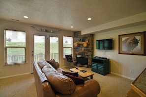 A living room with a leather sofa, a fireplace, a television, and a stone wall.