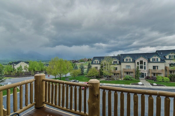 A residential area with a wooden deck railing, houses with multiple stories, and a cloudy sky.