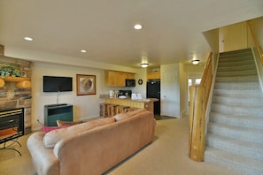 A living room with a sofa, a fireplace, a TV, and a kitchen area with a counter and stools.