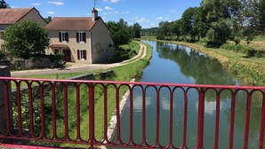 Ein Fluss mit einem Haus am linken Ufer und einem roten Geländer im Vordergrund.