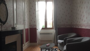 Ein Zimmer mit Kamin, einem Tisch mit Kerzen, einem Fenster mit Vorhängen und zwei Stühlen.
