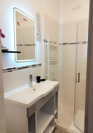 Un bagno con un lavandino bianco, uno specchio e una doccia.