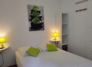 Ein Schlafzimmer mit einem Bett, zwei Kissen, einem Nachttisch mit Lampe, einem Wandregal und einem Gemälde.