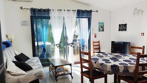 A hotel room with a sofa, a dining table with chairs, a TV, and a view of the outdoors through a window with sheer curtains. - Charming house Spa Terrace Garden (Angoulins)
