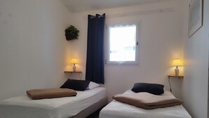A small, clean room with two beds, each with a pillow and a lamp on a bedside table. - Charming house Spa Terrace Garden (Angoulins)