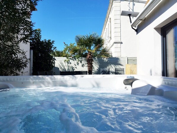 A hot tub in a courtyard with a white building, palm trees, and a clear blue sky.